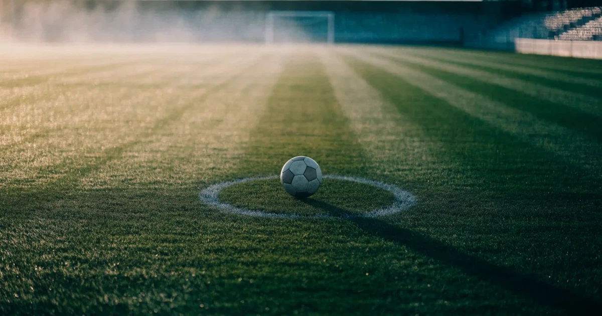 Un pallone da calcio sul dischetto del centrocampo di un prato, alla luce del mattino